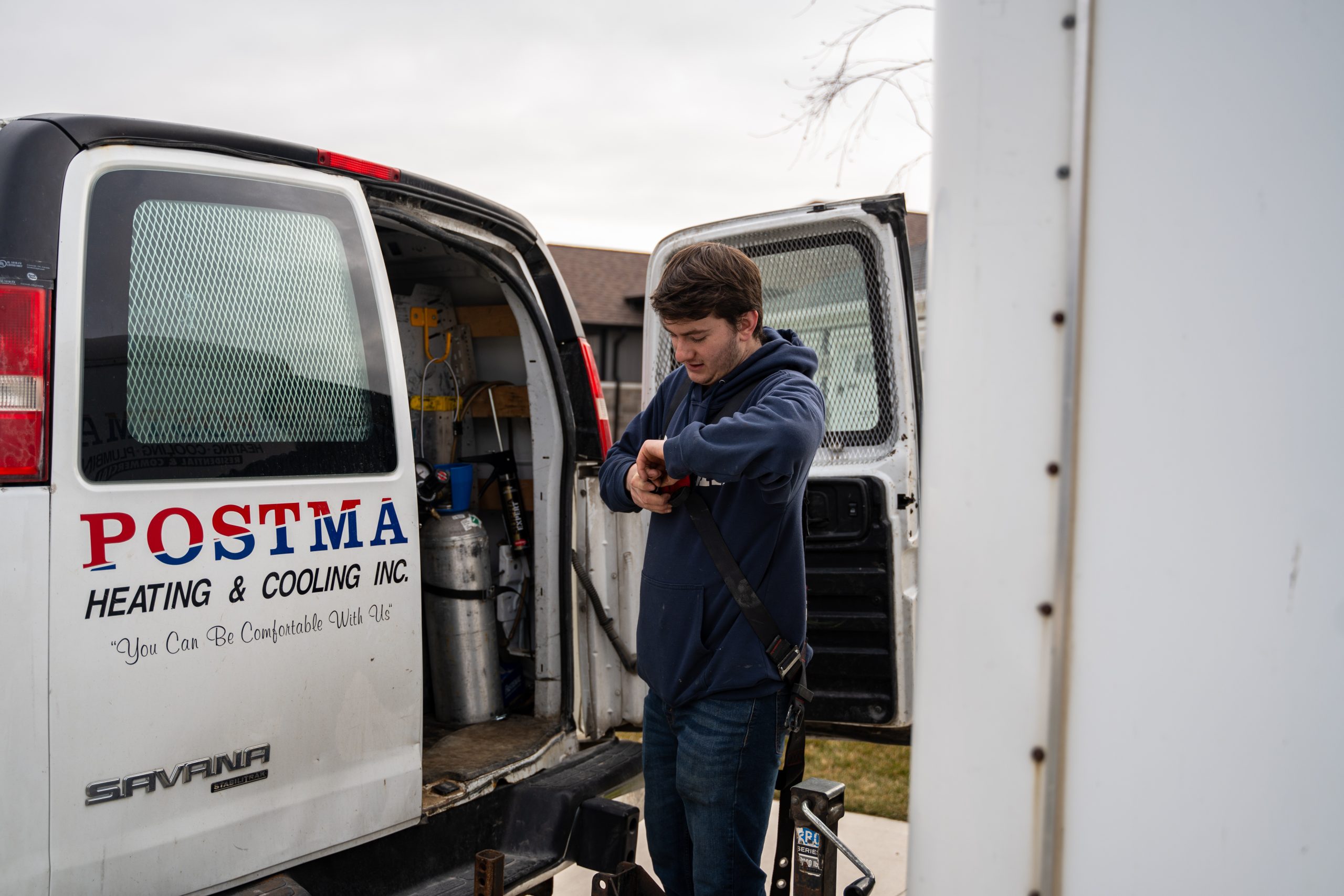Technician from Postma Heating & Cooling preparing equipment outside service van, emphasizing HVAC maintenance and reliability.