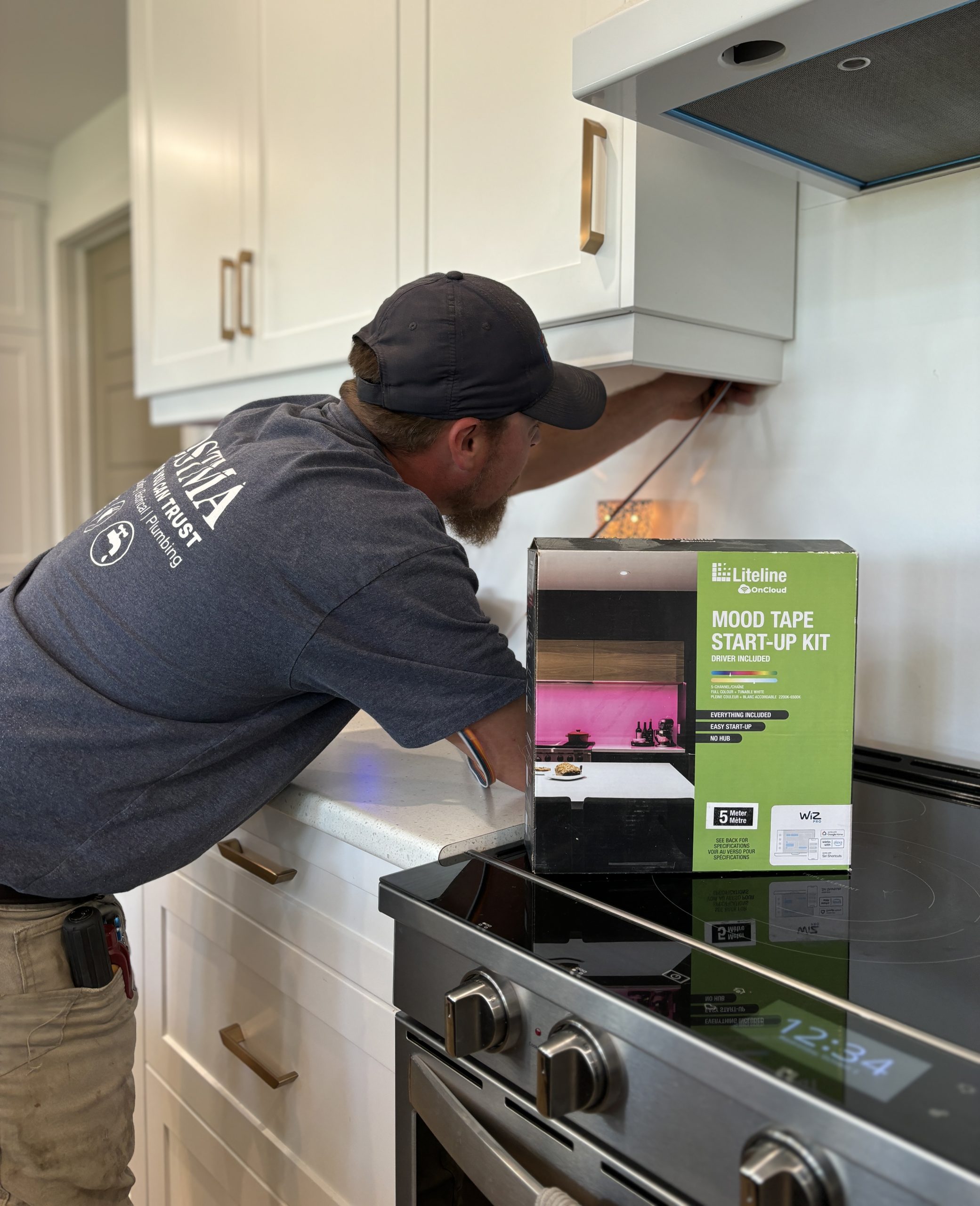 A skilled Postma electrician is installing under-cabinet lighting using a Liteline Mood Tape Start-Up Kit in a modern kitchen.