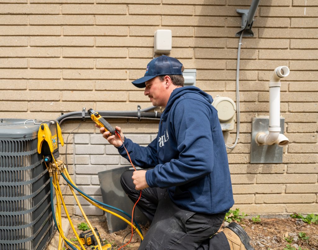 Technician using a multimeter to troubleshoot an air conditioning unit on a residential property.
