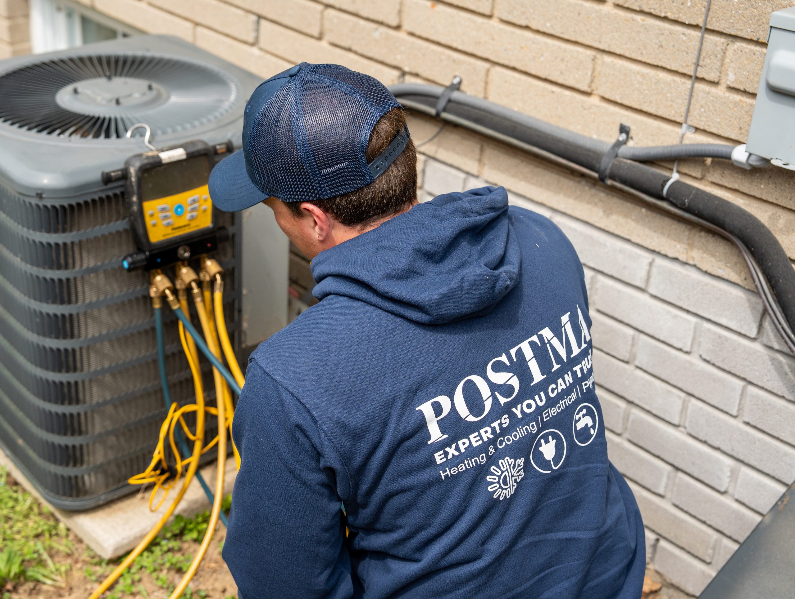 Technician in Postma hoodie servicing an air conditioning unit, showcasing AC maintenance expertise for local homes in Chatham-Kent.