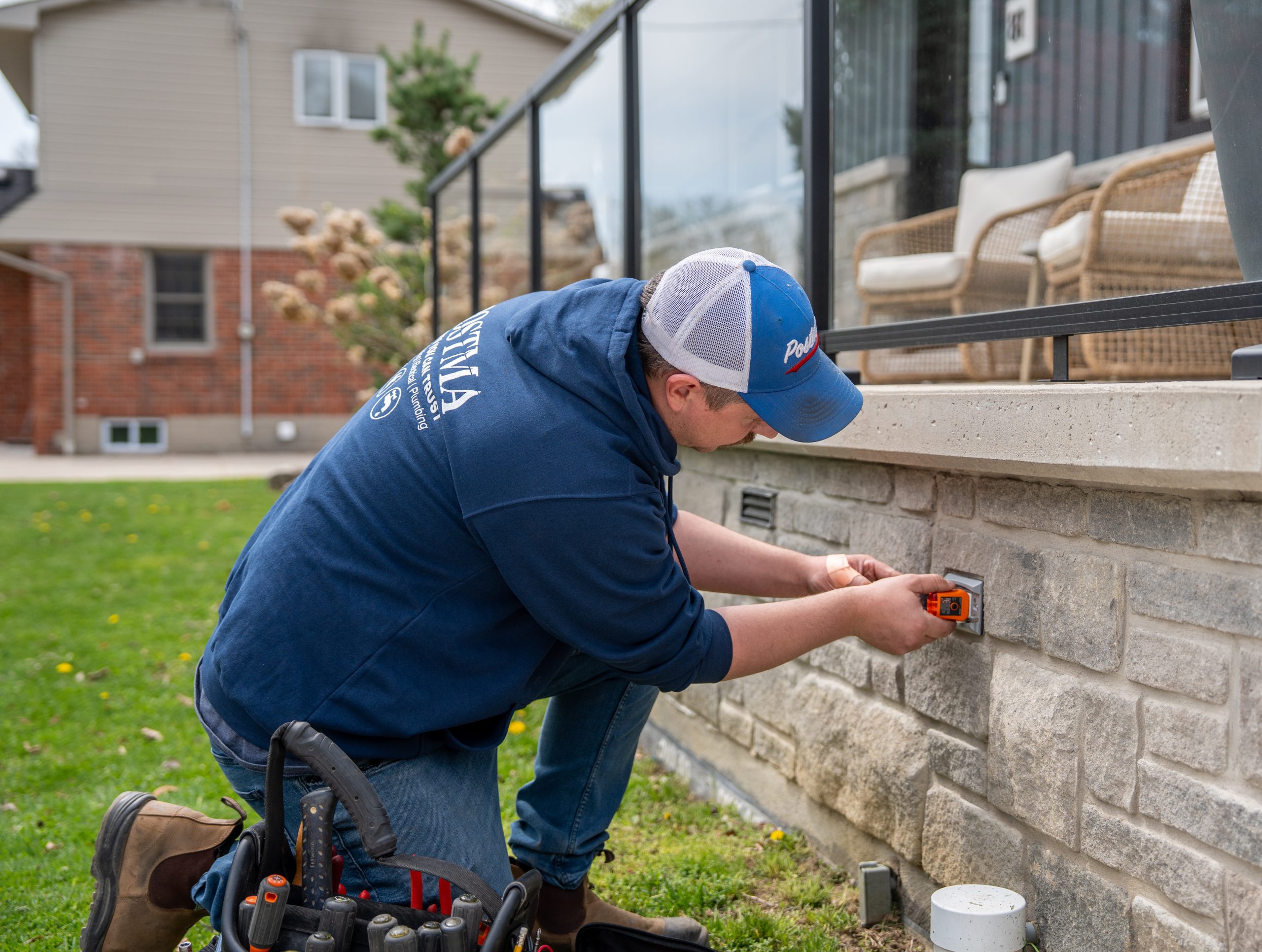 Technician from Postma Heating & Cooling using a laser level to install an electrical outlet on a stone wall outside a home in Chatham-Kent.