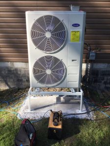 Carrier heat pump installed by Postma Heating, Cooling, Plumbing and Electrical outside a home in Chatham-Kent, Ontario, shown during installation on a raised stand.