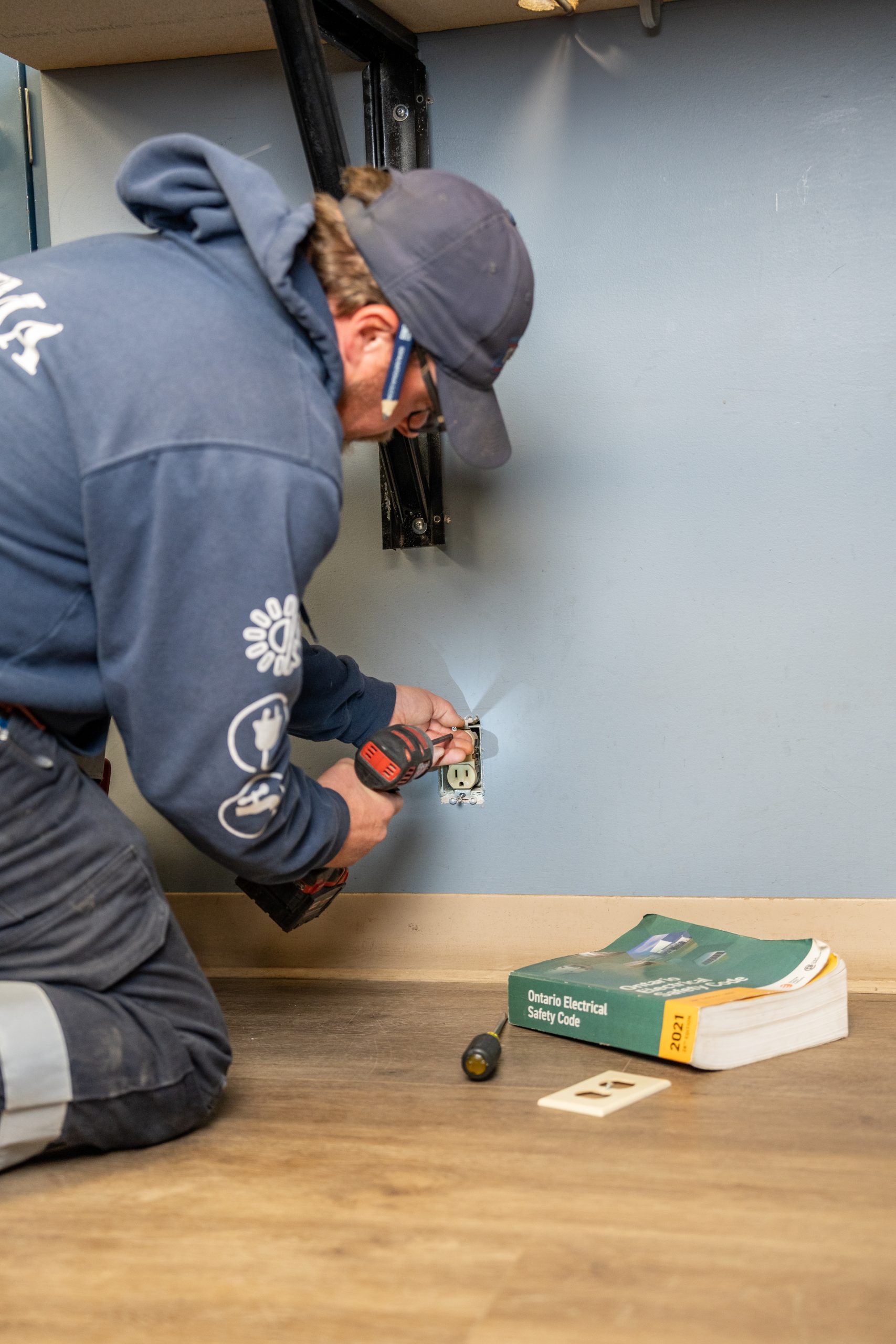 Licensed electrician installing an electrical outlet in a commercial office while referencing the Ontario Electrical Safety Code.