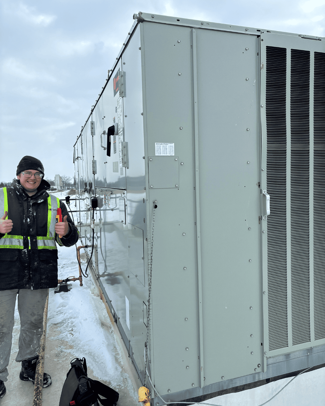 Commercial HVAC technician standing beside a rooftop HVAC unit after performing winter maintenance in Chatham-Kent.